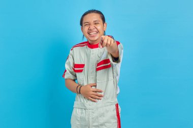 Mekanik üniforma giyen yakışıklı bir adamın portresi yüksek sesli kahkahalar atıyor, elleri karnında ve kamerayı işaret ediyor.