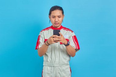 Mekanik üniforma giyen yakışıklı adam mavi arka planda cep telefonu kullanıyor.