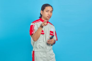 Mavi arka planda izole edilmiş cep telefonu kullanarak mekanik üniforma giyen kızgın yakışıklı bir adam.