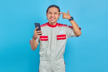 Cep telefonu tutan ve elinde sembolik silah tutan tamircinin portresi mavi arka planda el hareketleriyle izole edilmiş.