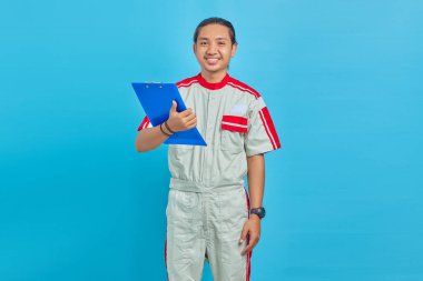 Gülümseyen yakışıklı tamirci elinde panoyla mavi arka planda izole edilmiş kameraya bakıyor.