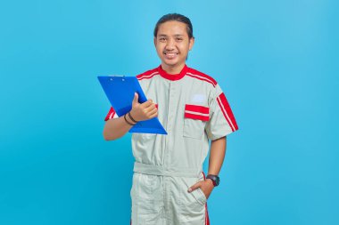 Gülümseyen yakışıklı tamirci elinde panoyla mavi arka planda izole edilmiş kameraya bakıyor.