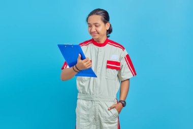 Mavi arka plandaki panoda iş listesine bakan gülümseyen genç ve yakışıklı tamircinin portresi