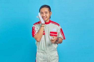 Mekanik üniforma giyen yakışıklı bir adamın portresi. Elinde doku tutan ve mavi arka planda izole edilmiş yüzünden ter silen bir adam.