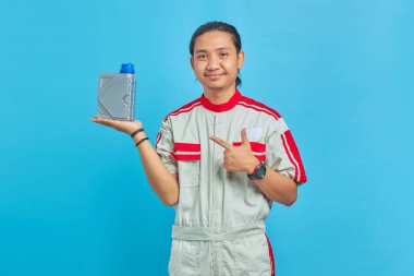 Motor yağı şişesini mavi arka planda gösteren, mekanik üniforma giyen neşeli yakışıklı adamın portresi.