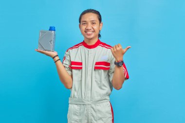 Motor yağı şişesini gösteren mekanik üniforma giyen neşeli yakışıklı bir adam portresi ve mavi arka planda boş bir alanı işaret ediyor.