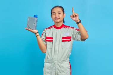 Mekanik üniforma giyen, motor yağı şişesini gösteren ve mavi arkaplanı işaret eden gülümseyen yakışıklı adamın portresi.