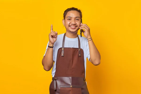 笑顔のアジアの若者の肖像スマートフォンや指を指して話している 黄色の背景 — ストック写真