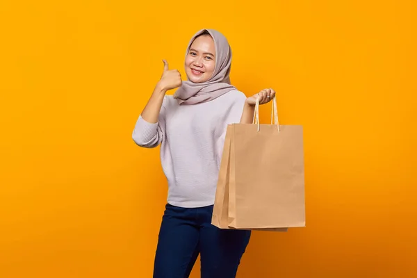 亚洲女人拿着购物袋 在黄色背景下竖起大拇指的形象 — 图库照片