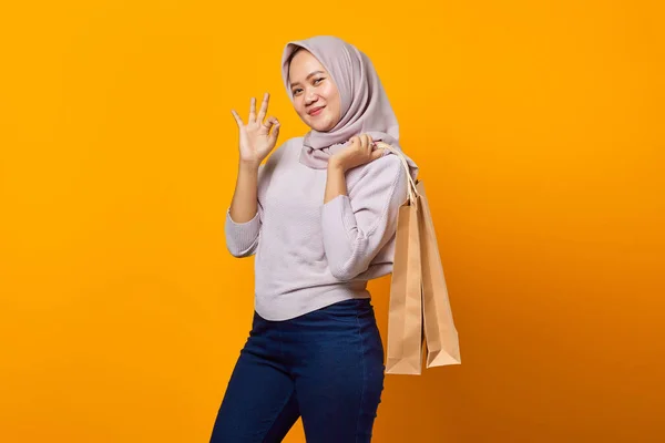 笑顔のアジアの女性の肖像ショッピングバッグを保持し 黄色の背景に指でOkサインを作る — ストック写真