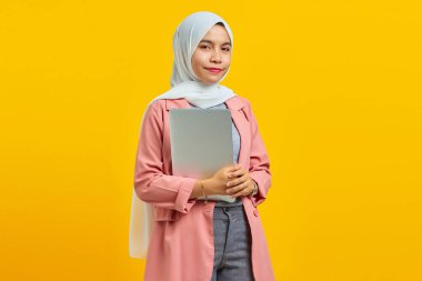 Sırıtkan Asyalı bir kadın dizüstü bilgisayarını sarı arka planda tutuyor.