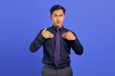 Kafası karışmış genç Asyalı adam mor arka planda kendini işaret ediyor.