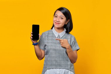 Gülümseyen Asyalı kadın boş akıllı telefon ekranı gösteriyor ve kameraya bakarken onu işaret ediyor.