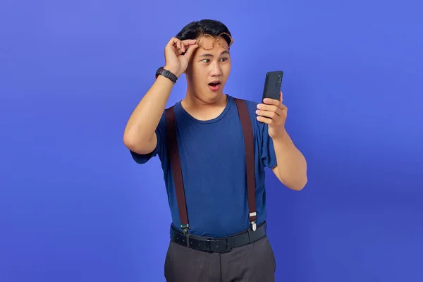 Σοκαρισμένος Νεαρός Που Χρησιμοποιεί Smartphone Και Βγάζει Γυαλιά Μωβ Φόντο — Φωτογραφία Αρχείου