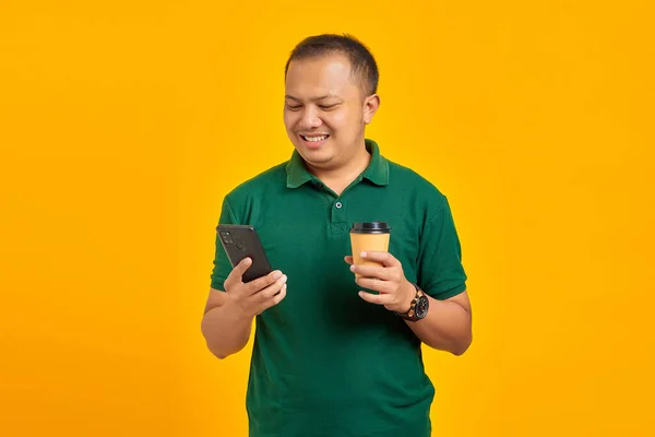 Молодий Азіат Користується Мобільним Телефоном Тримає Чашку Кави Ізольовану Жовтому — стокове фото