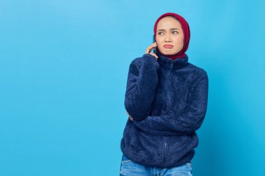 Cep telefonuyla konuşan kafası karışmış genç bir Asyalı kadın ve mavi arka planda izole edilmiş erkek arkadaşı.