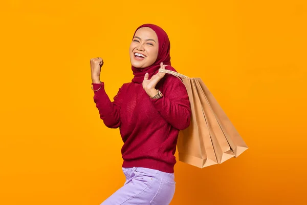 黄色の背景の上に意気揚々とした表情でショッピングバッグを保持興奮アジアの女性 — ストック写真
