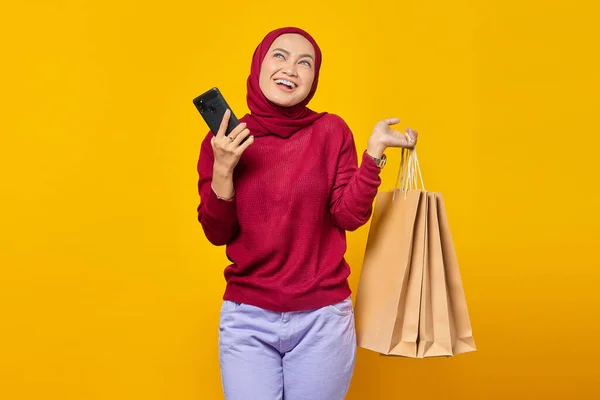 Mosolygó Fiatal Ázsiai Gazdaság Smartphone Bevásárló Táska Miközben Felnéz Sárga — Stock Fotó
