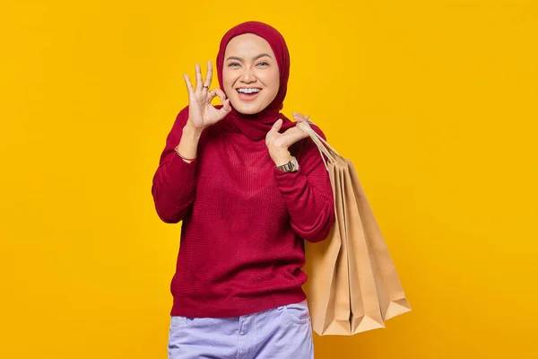 明るいアジアの女性の肖像ショッピングバッグを保持し 黄色の背景に指で大丈夫サイン — ストック写真