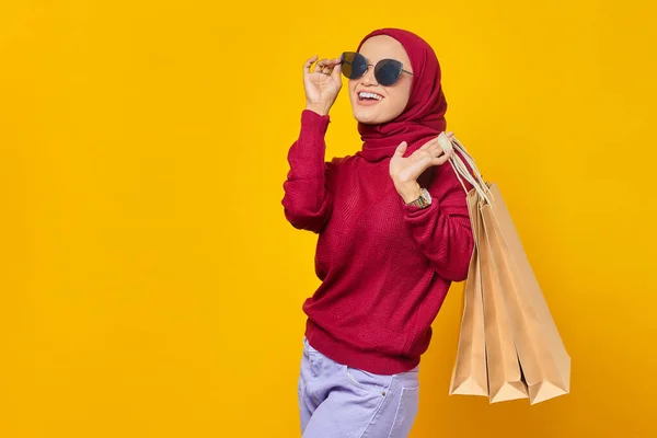 陽気若いアジアの女性はサングラスをかけ 黄色の背景にショッピングバッグを保持 — ストック写真