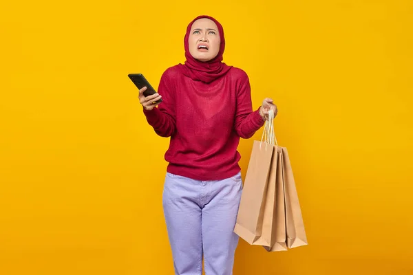 Удивлённая Молодая Азиатка Держит Мобильный Телефон Сумки Покупок Жёлтом Фоне — стоковое фото