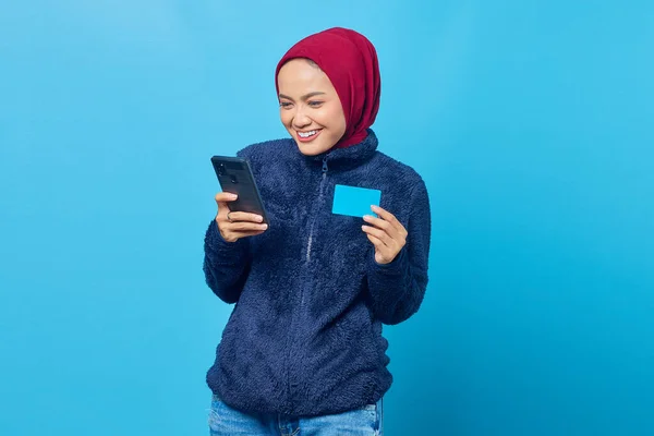 Веселая Молодая Азиатка Держит Мобильный Телефон Показывает Кредитную Карту Синем — стоковое фото