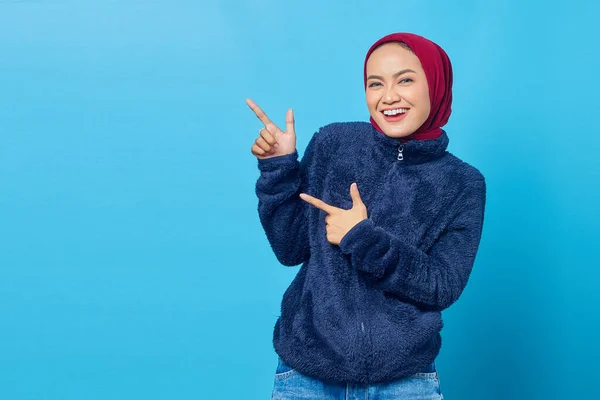 Portret Uśmiechniętej Młodej Azjatki Wskazującej Palcem Przestrzeń Niebieskim Tle — Zdjęcie stockowe