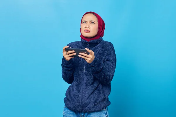 Шокированная Молодая Азиатка Играющая Видеоигру Смартфоне Смотрящая Синий Фон — стоковое фото