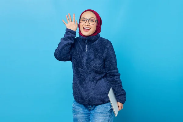 Hymyilevä Kaunis Opiskelija Jolla Kannettava Tietokone Vilkuttaa Kameralle Sinisellä Taustalla — kuvapankkivalokuva