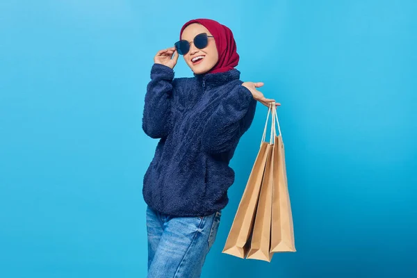 陽気若いアジアの女性はサングラスをかけ 青い背景にショッピングバッグを持っています — ストック写真