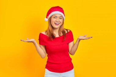 Neşeli genç Asyalı kadın Noel şapkası takıyor sarı arka planda merhaba demek için uzanıyor.