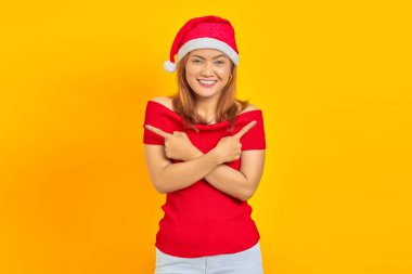 Genç Asyalı bir kadının portresi, Noel şapkası takıyor ve sarı arka plandaki fotokopi alanını işaret ediyor.