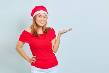 Neşeli, güzel Asyalı kadın Noel elbisesi giyiyor. Beyaz arka planda avuç içlerindeki fotokopi alanını gösteriyor.