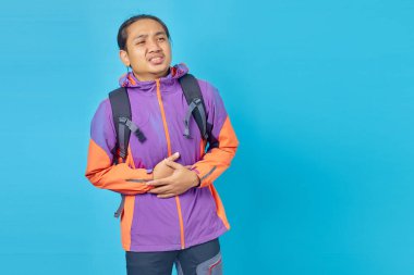 Portrait of anxious young Asian man suffering a painful stomach ache over blue background