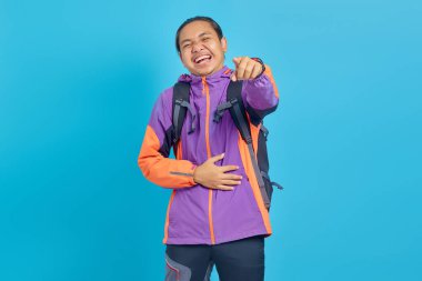 Portrait of handsome Asian young man laughing widely and pointing finger in front isolated on blue background