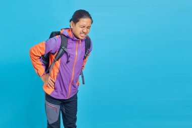 Portrait of handsome Asian man suffering from back pain and touching back with hands on blue background