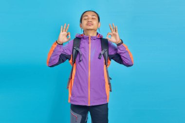 Portrait of handsome man smiling casually with closed eyes doing meditation gesture with finger over blue background