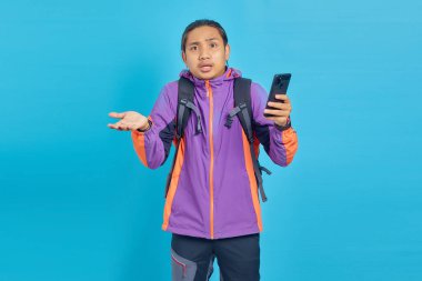Portrait of surprised young Asian man holding on mobile phone with open mouth isolated on blue background