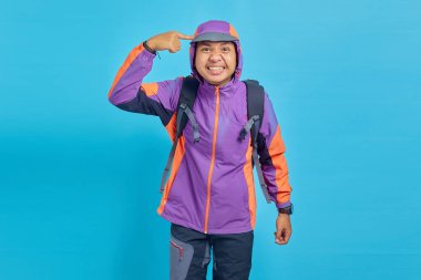 Portrait of angry Asian young man pointing head with finger and gesturing for thought isolated on blue background