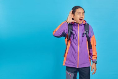 Portrait of Asian man eavesdropping on conversation isolated on blue background