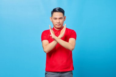 El ele tutuşan Asyalı genç bir adamın portresi dur hareketi yapıyor, mavi arka planda izole edilmiş reddedilmeyi gösteriyor.