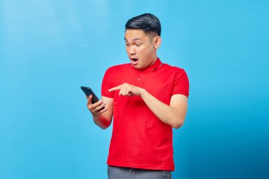 Mavi arka planda akıllı telefon kullanan ve mesajlaşan yakışıklı Asyalı genç adamın portresi