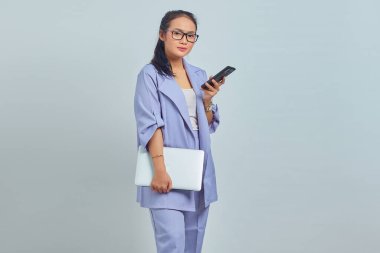 Laptop tutan ve beyaz arka planda izole cep telefonu kullanan düşünceli genç Asyalı kadının portresi