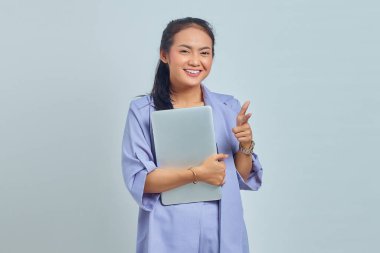 Dizüstü bilgisayarını tutan ve beyaz arka planda izole edilmiş kamerayı gösteren gülümseyen Asyalı genç kadının portresi.