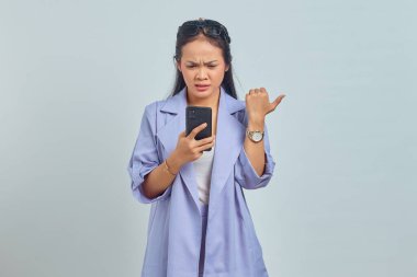 Cep telefonundan gelen mesaja bakıp beyaz arkaplanda izole edilmiş kopya alanına işaret eden mutsuz Asyalı genç kadının portresi