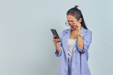 Beyaz arka planda ağzı açık bir şekilde telefon ekranına bakan Asyalı genç bir kadının portresi.