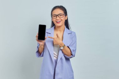 Beyaz arka planda izole edilmiş boş ekran cep telefonuna işaret eden gülümseyen Asyalı genç kadın portresi