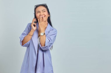 Beyaz arka planda ağzı kapalı, cep telefonuyla konuşan neşeli Asyalı genç kadının portresi.