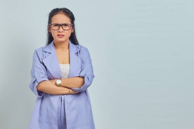 Kollarını kavuşturup beyaz arka planda izole edilmiş kameraya bakan şaşırmış Asyalı genç bir kadının portresi.