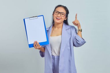 Gülümseyen Asyalı genç iş kadınının portresi boş pano gösteriyor ve mor arkaplanda parmak izolasyonu olan kopya alanını işaret ediyor